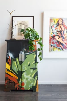 a plant sitting on top of a wooden cabinet next to a painting and framed pictures