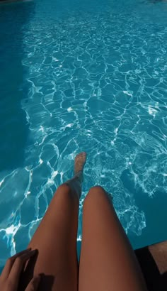 a woman's legs are in the water near a swimming pool with clear blue water