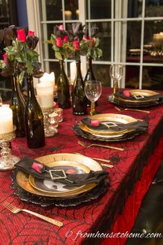 the table is set with black and gold place settings, wine bottles, candles, and roses