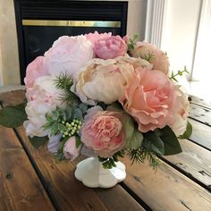 a vase filled with pink and white flowers on top of a wooden table next to a fireplace