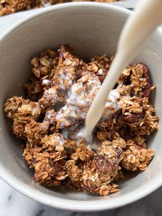 a bowl filled with granola and milk being poured into it