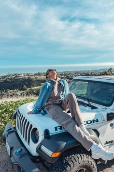 a man sitting on top of a white jeep in front of the ocean with sunglasses on