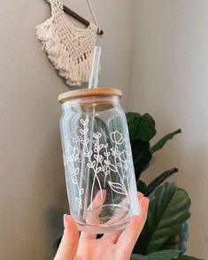 a person holding up a clear glass jar with white flowers on the inside and wooden lid