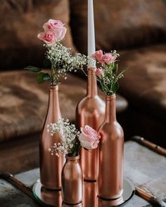 three copper vases with pink roses and baby's breath are on a tray