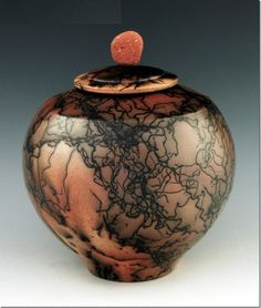 a brown and black vase with a red lid