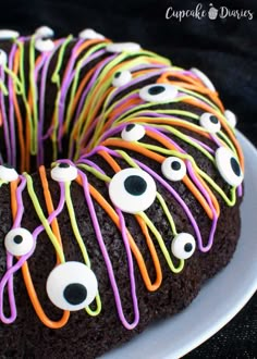 a chocolate cake decorated with googly eyes and neon colored icing on a white plate