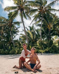 two people sitting on the beach with palm trees in the background