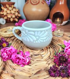 a white cup sitting on top of a wicker table next to vases and flowers