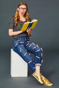 a woman sitting on top of a white block holding a book and making a funny face