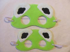 two green masks with white and black eyeballs on them sitting on a cloth surface