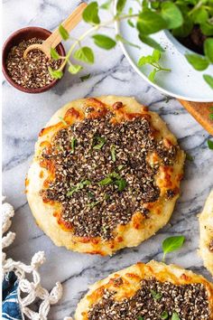 two small pizzas on top of a marble counter next to a bowl of greens