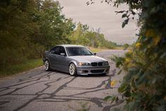 a silver car parked on the side of a road next to some bushes and trees