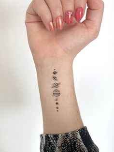 a woman's hand with a small tattoo on her left wrist and planets in the background