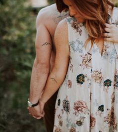 a man and woman holding hands while standing next to each other in front of trees