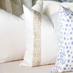 two white pillows sitting on top of a couch next to each other with blue and white designs