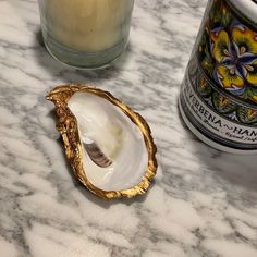 an open shell sitting on top of a marble counter next to a jar and candle