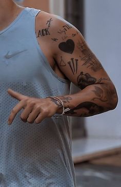 a man with tattoos on his arm pointing at something in the air while wearing a blue tank top