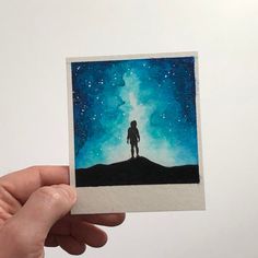 a hand holding up a piece of paper with an image of a person standing on top of a hill