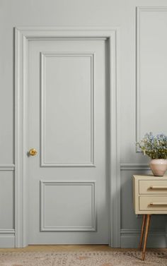 an empty room with a white door and some flowers on a small table next to it