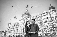 a man and woman standing next to each other in front of a building with birds flying overhead