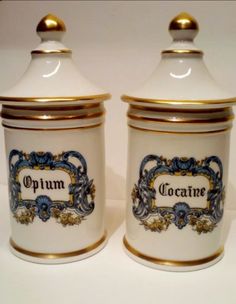 two white and gold canisters with ornate designs on the sides, one is empty