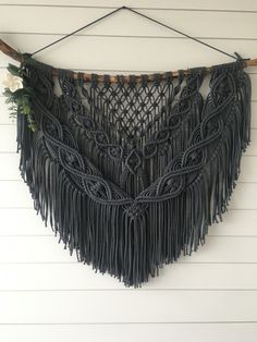 a black macrame hanging on the wall next to a white wall with flowers