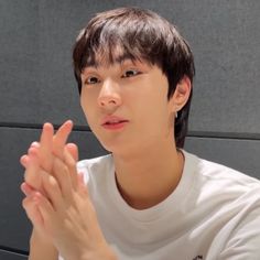 a young man sitting in front of a wall holding his hands together