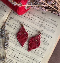 two red crocheted heart shaped earrings sitting on top of an old sheet of music