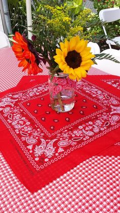 sunflowers are in a vase on a red tablecloth with white checkered table cloth