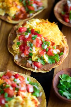 some tacos are sitting on a table with salsa and cilantro in the middle