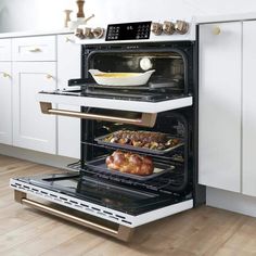 two open ovens in a kitchen with white cabinets and wood flooring, one has food on the bottom shelf