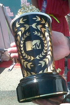 a person holding up a cup that is decorated with gold and black designs