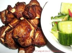 some meat and vegetables on a white plate next to a bowl of salad with cucumbers