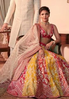 a man standing next to a woman in a red and yellow lehenga set