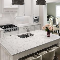 a kitchen with white cabinets and marble counter tops, two pendant lights over the sink