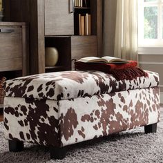 a brown and white cow print footstool sitting in front of a bookcase