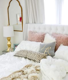 a white bed topped with pillows and blankets next to a mirror on the wall above it