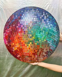 a person holding up a large colorful mosaic mirror ball in front of a white backdrop