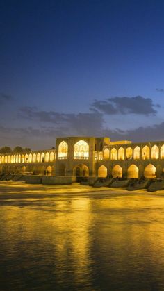 a large building sitting on the side of a river at night with lights reflecting in the water