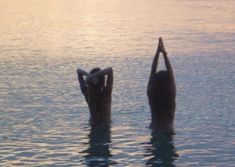 two people are standing in the water doing yoga poses with their hands behind their backs