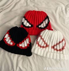 three knitted hats are laying on top of a white sheet, one is red and the other is black