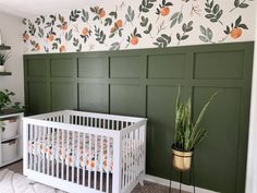 a baby's room with green paneled walls and a white crib next to a potted plant