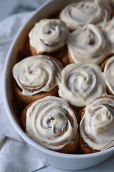 a white bowl filled with cinnamon rolls covered in frosting on top of a table