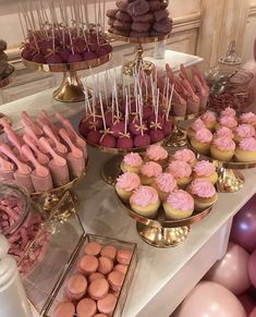 a table topped with lots of cupcakes and desserts covered in pink frosting