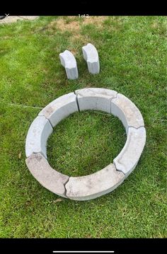 a circular stone fire pit sitting on top of a green grass covered field next to three cement blocks