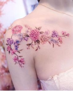 the back of a woman's shoulder with pink and purple flowers tattooed on it