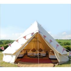 a large tent with two beds in it on the grass near some trees and bushes