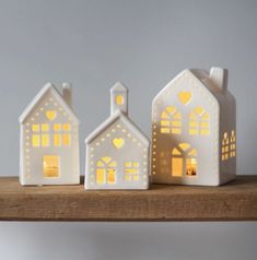 three small white houses sitting on top of a wooden shelf with lights in the windows