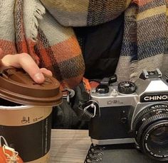 a person holding a coffee cup next to a camera and a pumpkin on a table