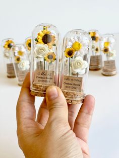 a hand is holding small glass vases with sunflowers and daisies in them